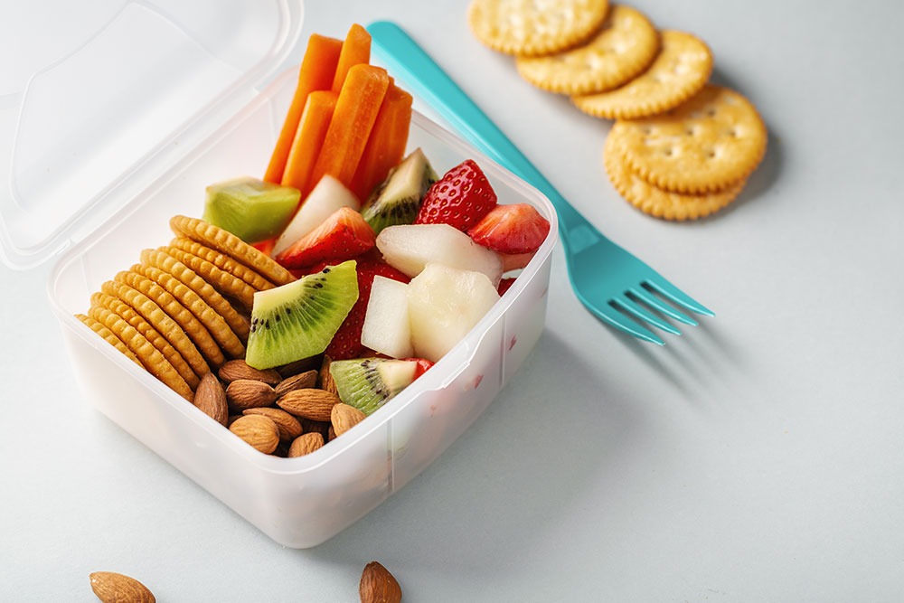 A lunch box filled with crackers, fruit, and nuts.