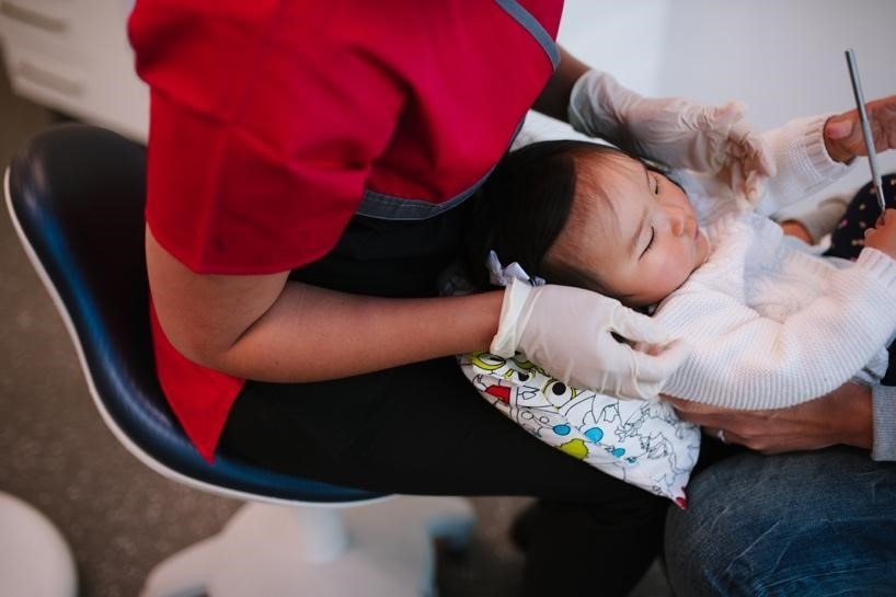 Child sitting in mother's lap as dentist examines her for dental trauma.