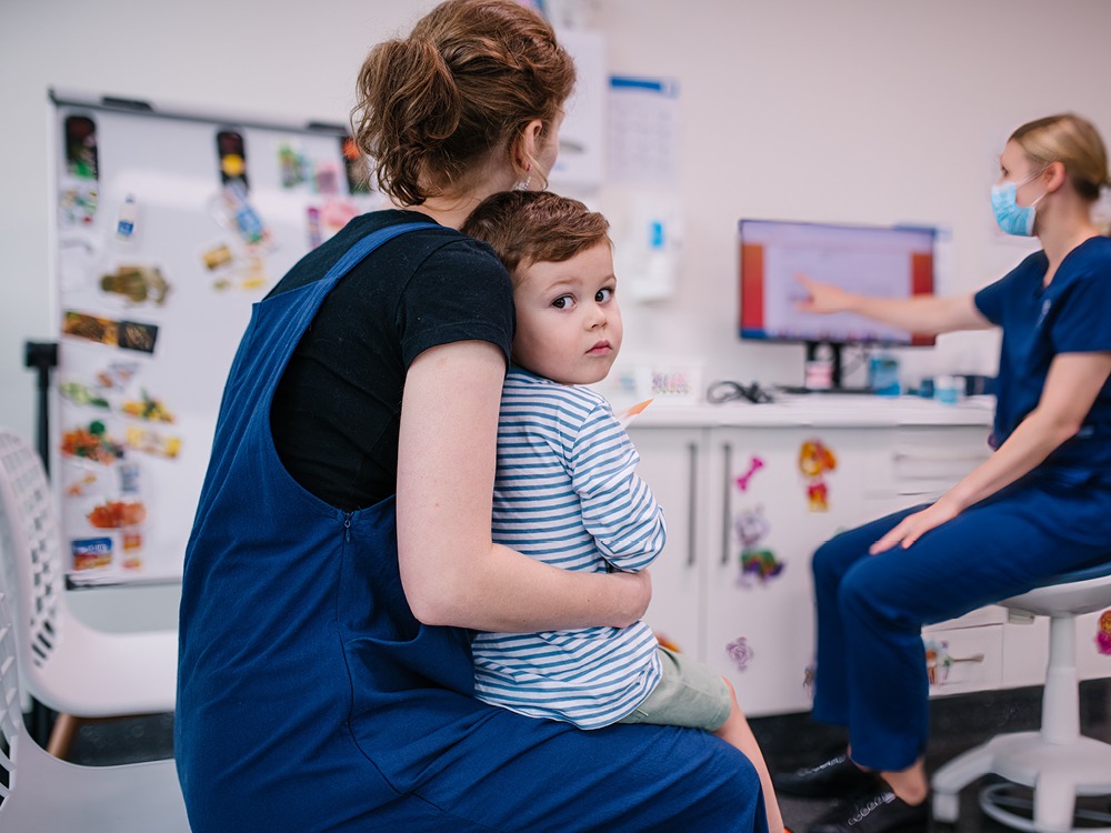 A small boy sitting on his mother's lap at the dentist, looking at the camera with a worried expression.